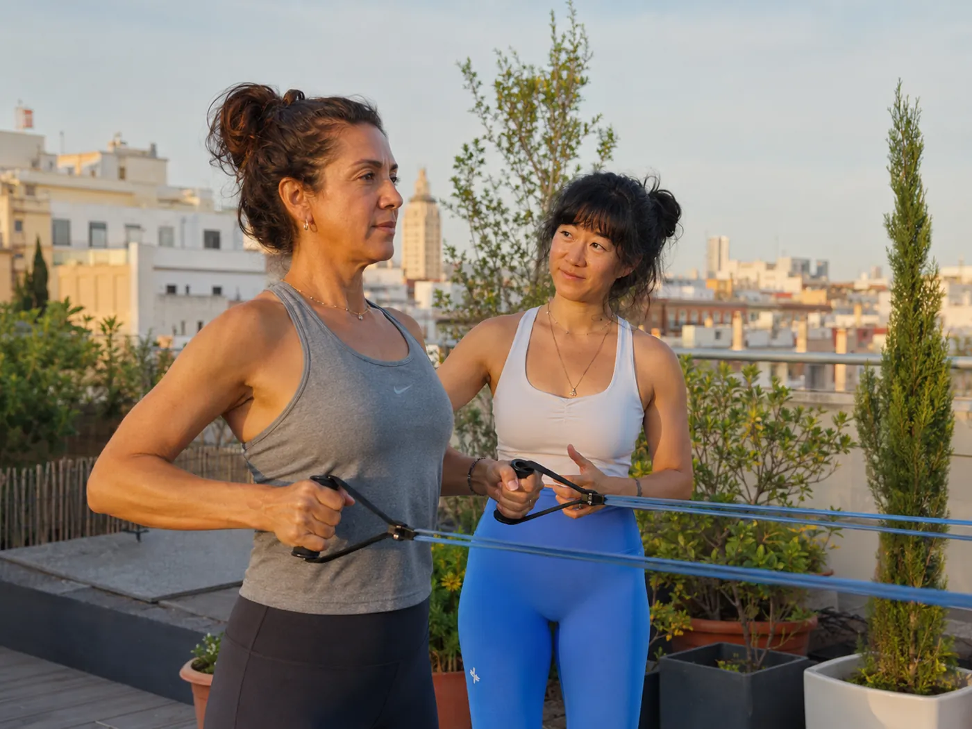 Julie coaching a woman through a resistance band exercise on a rooftop